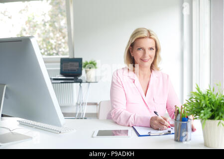 Beautiful elderly businesswoman sitting at desk and doing some paperwork. Stock Photo