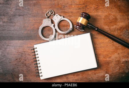 Law and order concept. Handcuffs, gavel and a notebook on a wooden background with copy space. Stock Photo