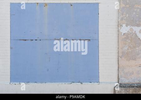 Whitwashed old brick wall with blue borded up window Stock Photo