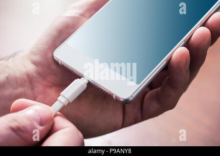 White USB Cable Connected With A White Mobile Phone, Holded By Male Hands Stock Photo