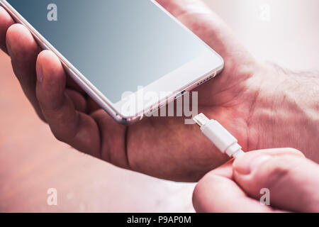 Plugging In A White USB Cable In A White Smartphone By Male Hands Stock Photo