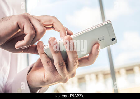 Macro Of A Businessman In White Shirt Using A White Mobile Phone In Front Of A Bright Background Stock Photo