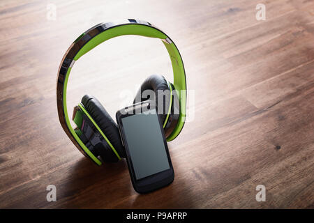 Wireless Listen To Music Concept With A Smartphone Leaning On A Big Black Overhead Headphone On Wooden Table Stock Photo