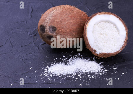 Fresh ripe coconuts on black slate. Heap of coconut flakes on dark background. Healthy exotic fruit. Stock Photo