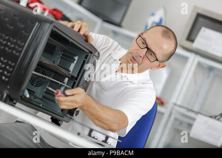 repairman working on a microwave in the kitchen Stock Photo