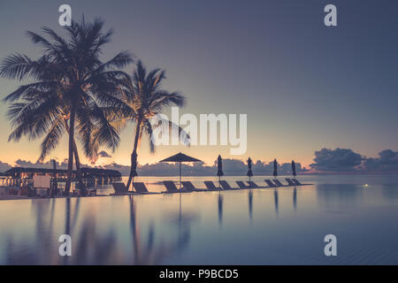Luxury infinity beach pool in sunset time. Palm trees and calm weather on the beach. Summer vacation and holiday concept Stock Photo