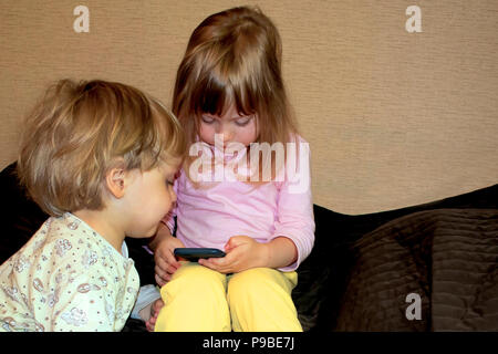 Little cute curious blonde twins watch cartoons on smartphone Stock Photo