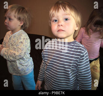 One of little cute triplets posing in front of camera, other two in the background Stock Photo