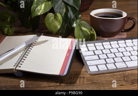 Opened notebook and pen on a wooden desktop with computer keyboard and cup of coffee Stock Photo