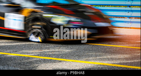 Motor sport car racing on asphalt road with blue fence and yellow line traffic sign. Car with fast speed driving and motion blurred. Black racing car  Stock Photo