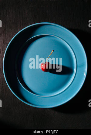 Single cherry on a blue plate, in studio, dark food photography Stock Photo