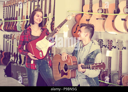 Teenage girl and boy are choosing between acoustic and electric guitar in guitar shop. Stock Photo