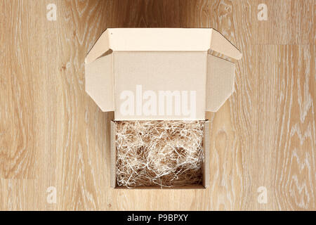 Opened cardboard box with wood excelsior shred filler on wooden background. View above Stock Photo