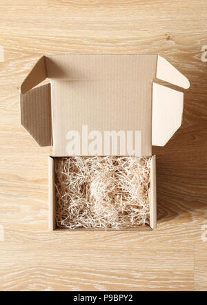 Opened cardboard box with wood excelsior shred filler on wooden background. View above Stock Photo