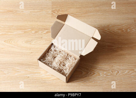 Opened cardboard box with wood excelsior shred filler on wooden background. View above Stock Photo