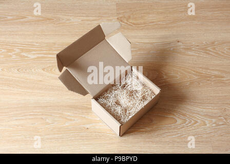 Opened cardboard box with wood excelsior shred filler on wooden background. View above Stock Photo