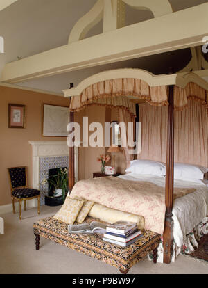 Pale pink drapes and quilt on a four poster bed in a large country bedroom Stock Photo