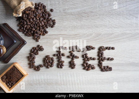 top view Coffee beans on wooden background in form of word of "coffee", grinder and sack in background Stock Photo