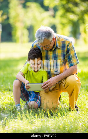 Grandfather and grandson using digital tablet in park Stock Photo