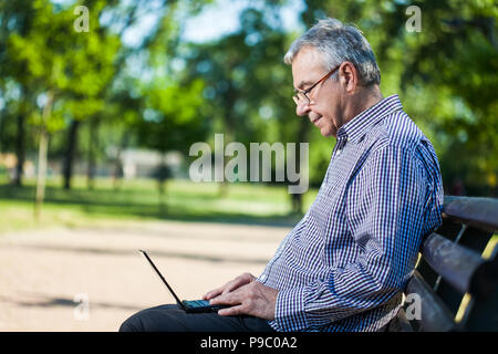 Senior man using laptop in park Stock Photo