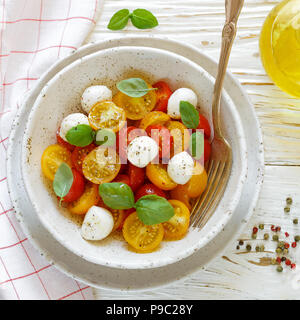 Delicious summer salad of yellow and red cherry tomatoes, mozzarella with Basil and spices. Caprese. Selective focus and square picture Stock Photo