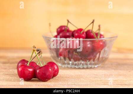 bowl of red cherries and in the foreground five cherries, everything is on a wooden surface Stock Photo