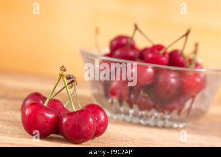 bowl of red cherries and in the foreground five cherries, everything is on a wooden surface Stock Photo