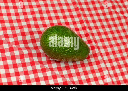 Whole avocado on red checkered tablecloth Stock Photo
