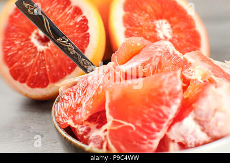 Detail photo - peeled grapefruit cut into pieces in small bowl with spoon, with whole citrus in background. Stock Photo