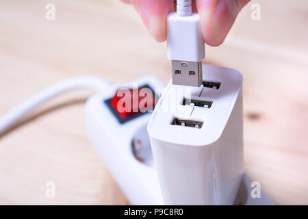 Connecting A White USB Cable To A White USB Charger Which Is Plugged Into A Power Strip Stock Photo