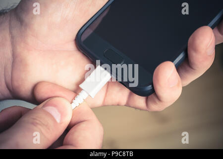 Plugging Out A White USB Cable Connected With A Black Mobile Phone, Holded By Male Hands Stock Photo