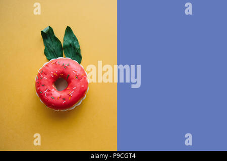 A creative donut with ears of leaves resembling a rabbit on a colored background in a minimal style. Nearby place for text. Stock Photo