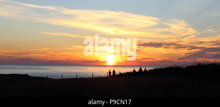 Watching the Sunset. People gather on a clifftop in Northern Ireland to watch the sun set over the North Atlantic from the causeway coast. Stock Photo