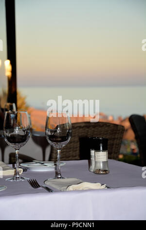 Sun set over sea with table set for dinner and wine glasses Stock Photo
