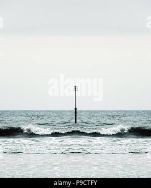Waves and surf breaking onto a beach around a groyne beacon, England UK - symmetry concept Stock Photo
