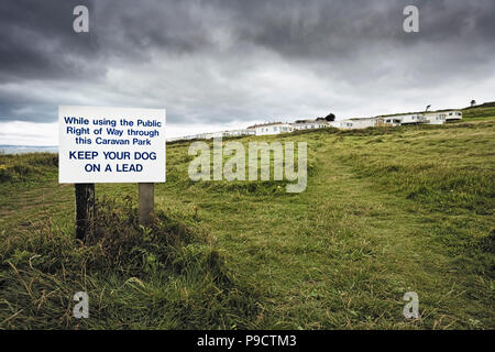 Warning sign and traditional British mobile home or static caravan holiday park on the clifftop at Burton Bradstock, Dorset, England, UK Stock Photo