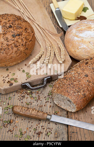 Seeded breads and a white loaf on a bread board with wheat and a bread knife. UK Stock Photo