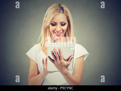Pretty blond woman in casual outfit using modern new tablet and smiling on gray background Stock Photo