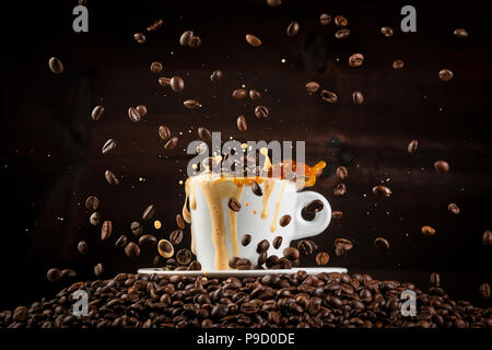 White ceramic cup of coffee with splashes and falling coffee beans on heap of grains against black background Stock Photo