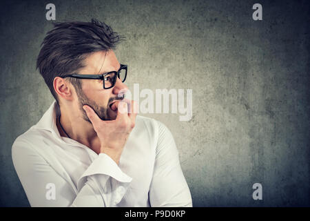 Adult bearded man having panic and phobia looking away while biting nails in anxiety on gray background Stock Photo