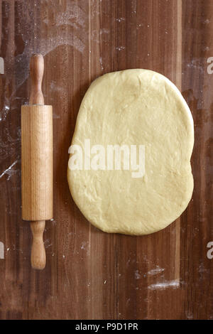 Making homemade pizza in a country kitchen with an overhead view of rolled out dough for the base with a wooden rolling pin on oven paper on an old wo Stock Photo