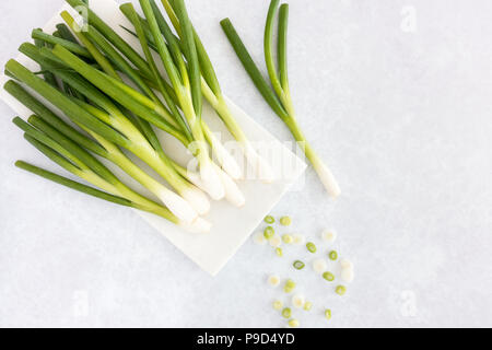 Top view of whole spring onions with water drops on a white marble chopping board and cut spring onions on a trendy  grey patterned background. Stock Photo