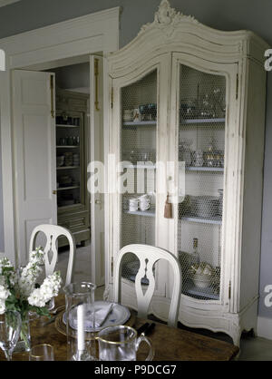 White painted glass front cupboard in a pale grey dining room with white painteds chairs Stock Photo