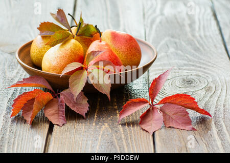 Pears. Collecting pears. Fresh ripe pears in a clay plate with autumn leaves on a wooden table. Pear autumn harvest. The concept of autumn nature. Stock Photo