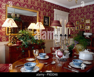 Lighted lamps on sideboard below mirror in a nineties living room with red patterned wallpaper Stock Photo