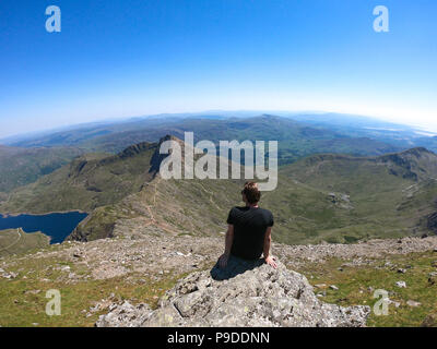 A hiker looks out  from the summit of Mount Snowdon, Wales, UK. Mount Snowdon stands at 1,085 Meters above sea level. Stock Photo