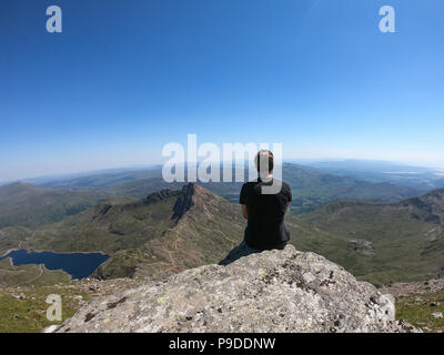 A hiker looks out  from the summit of Mount Snowdon, Wales, UK. Mount Snowdon stands at 1,085 Meters above sea level. Stock Photo