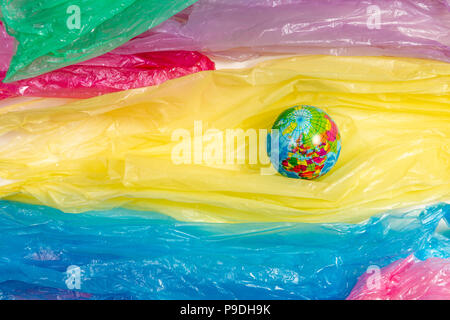 Small globe between a heap of plastic bags. Plastic excessive use problem concept. Stock Photo