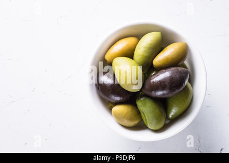 Black and green olives in a bowl on white marble table. Top view with space for text. Stock Photo