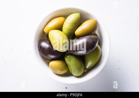 Black and green olives in a bowl on white marble table. Top view. Stock Photo